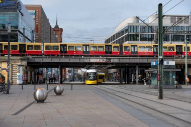 Almanya 24 Mart 2024. Bir binanın önündeki raylarda kırmızı ve sarı bir tren var. Tren birkaç kişi ve birkaç bisikletle çevrilidir.