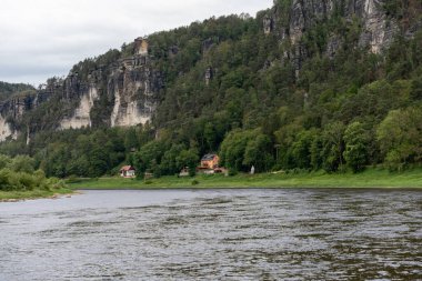 Sahilde evi olan bir nehir. Ev küçük ve kahverengi. Su sakin ve berrak.