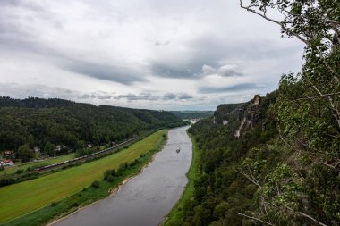 Trenin geçtiği bir nehir. Gökyüzü bulutlu ve ağaçlar yeşil