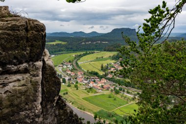 İçinden nehir akan bir kasaba manzarası. Kasaba tepelerle çevrili ve gökyüzü bulutlu.