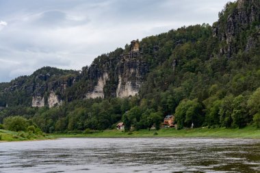 Sahilde evi olan bir nehir. Ev kırmızı ve bir bacası var. Su sakin ve gökyüzü bulutlu.