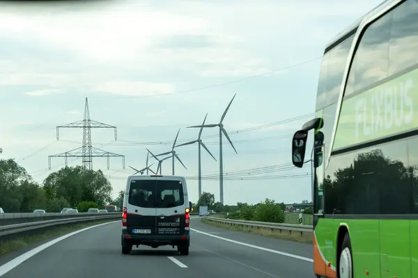 stock image Germany, May 17, 2024. A green bus is driving down a road next to a white van. The sky is cloudy and the road is empty