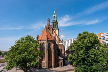 Çan kulesi ve saat kulesi olan büyük bir kilise. Binanın etrafı ağaçlarla çevrili ve yeşil bir çatısı var. Gökyüzü açık ve mavi