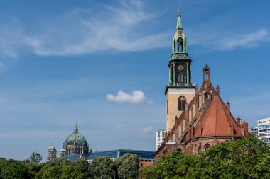 Uzun bir çan kulesi ve tepesinde kubbesi olan bir kilise. Gökyüzü mavi ve bazı bulutlar var.