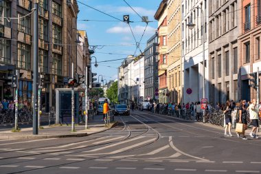 Almanya 17 Mayıs 2024, kalabalık bir şehir caddesi. Yürüyen ve bisiklete binen birçok insan var. Sokak binalarla dolu ve yoğun trafik var..