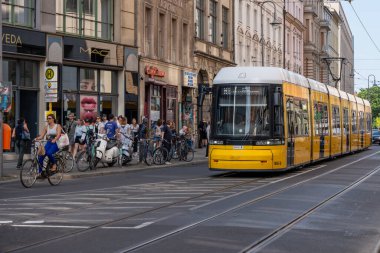 Almanya 17 Mayıs 2024. Birçok insanın bisiklete bindiği ve yürüdüğü bir caddenin yanındaki yolda sarı ve siyah bir tren var..