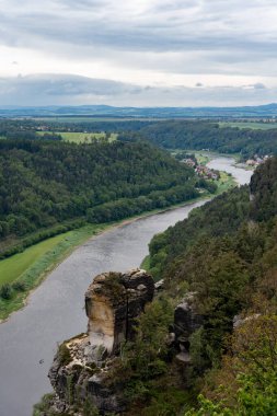 Arka planda dağ olan bir vadi boyunca bir nehir akar. Gökyüzü bulutlu ve sahne huzurlu.