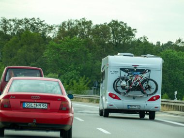 Almanya 17 Mayıs 2024 tepesinde bisiklet parkı olan beyaz bir kampçı yolda ilerliyor. Arkasında kırmızı bir araba var.