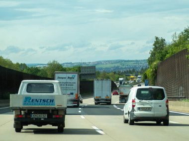 Almanya 17 Mayıs 2024 Yoğun Otoyol, yanında harfler olan beyaz minibüs. Yolda bir kamyon ve bir araba da dahil olmak üzere birkaç araç daha var. Bulutlu gökyüzü