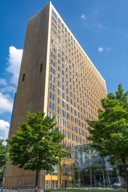 Önünde bir sürü pencere ve bir ağaç olan büyük bir bina. Bina kahverengi ve modern görünümlü.