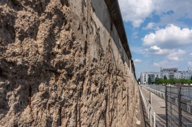 Eski Berlin Duvarı. Bir sürü çatlağı ve deliği olan bir duvar. Duvar betondan yapılmış ve çok pürüzlüdür. Gökyüzü bulutlu ve güneş parlıyor