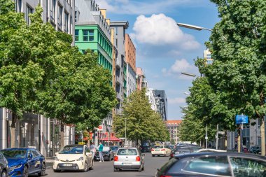 Almanya 7 Haziran 2024 Arabaları ve yayaları olan işlek bir şehir caddesi. Sokaklar ağaçlar ve binalarla dolu, ona canlı ve hareketli bir atmosfer sağlıyor.