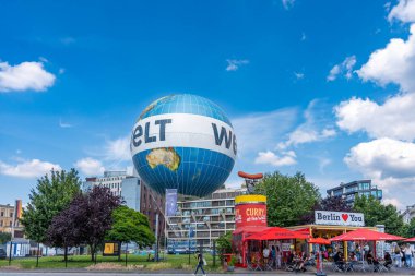 Almanya 7 Haziran 2024. Üzerinde harfler olan büyük mavi ve beyaz bir küre. Küre kırmızı yazıtlı bir binanın önündedir. Bölgede birkaç kişi var.