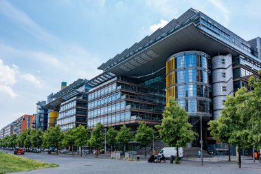 Almanya, 7 Haziran 2024. Önünde bir sürü pencere ve yeşil ağaç olan büyük bir bina. Bina ağaçlar ve arabalarla çevrili.