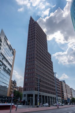 Bir sürü penceresi ve kırmızı çatısı olan yüksek bir bina. Gökyüzü mavi ve bulutlar var