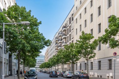 Almanya, 7 Haziran 2024 Ağaçlar ve binalarla dolu bir cadde. Sokaklar arabalar ve insanlarla dolu. Manzara canlı ve hareketli.