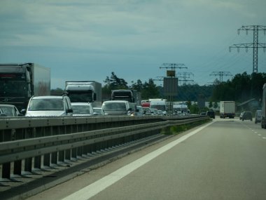 Almanya 17 Mayıs 2024 Birçok araba ve kamyonun bulunduğu işlek bir otoyol. Arabalar trafikte durduruldu ve kamyonlar ters yönde ilerliyor. Gökyüzü bulutlu ve güneş parlıyor