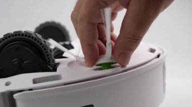 Bir insan bir robot üzerinde çalışıyor. Robot beyaz ve tekerlekleri var.
