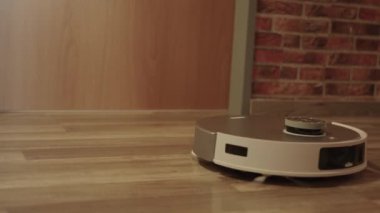 Ahşap bir zeminde bir robot duruyor. Robot beyaz ve siyah bir kafası var.