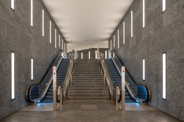 Büyük, boş, modern görünümlü, gri beyaz metro istasyonu ve iki yürüyen merdiven. Yürüyen merdivenler istasyonun sol ve sağ tarafında.