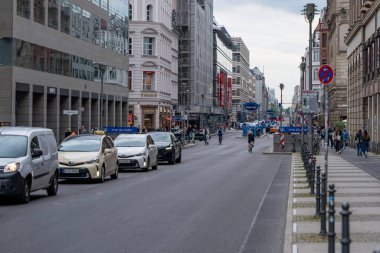 Almanya 14 Haziran 2024 yoğun bir şehir caddesi. Trafik ve yayalar var. Sokak yüksek binalarla dolu ve kaldırım kenarında park edilmiş bir sürü araba var.