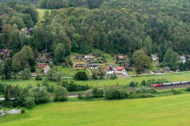 Küçük bir kasabanın yanındaki raylardan bir tren geçiyor. Tren kırmızı ve siyah.