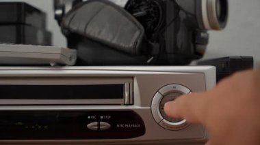 Uzaktan kumandanın yanındaki masada gümüş ve siyah bir VCR duruyor.