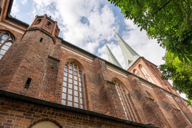 Yeşil çatılı ve yüksek kuleli büyük bir tuğla bina. Binanın bir sürü penceresi ve çan kulesi var.