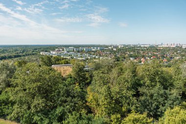Tepenin tepesinden bir sürü ağacın olduğu bir şehir manzarası. Ağaçlar yeşil ve gökyüzü mavi.