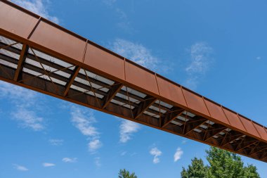 Arka planda mavi gökyüzü olan bir köprü. Köprü metalden yapılmıştır ve bir sürü açık alanı vardır.