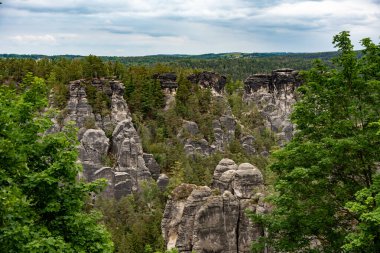 Arkasında orman olan bir dağ sırası. Ağaçlar yeşil ve gökyüzü bulutlu