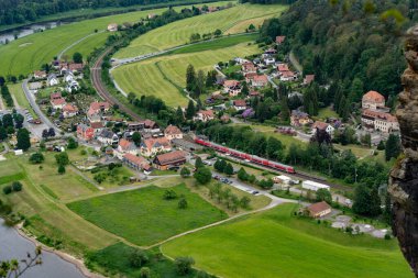 Bir tren arka planda evleri ve nehri olan küçük bir kasabadan geçiyor. Tren kırmızı ve olay yerinde sadece o görünüyor.