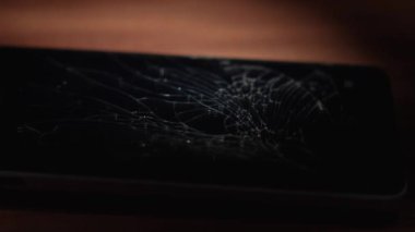 Kırık bir akıllı telefon ahşap bir masada yatıyor ve polisin yanıp sönen ışıkları kırık ekrana yansıyor. Kırık telefon, yakın plan..