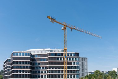 Büyük bir binanın yanında uzun bir vinç duruyor. Vinç sarı ve gökyüzünün ortasında.