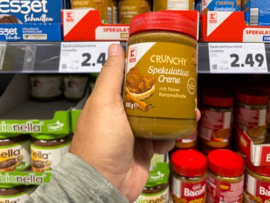 Adamın biri süpermarkette fıstık ezmesi kavanozu tutuyor. Çeşitli ürünler mevcuttur.