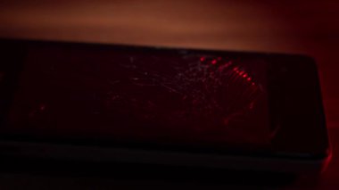 Kırık bir akıllı telefon ahşap bir masada yatıyor ve polisin yanıp sönen ışıkları kırık ekrana yansıyor. Kırık telefon, yakın plan..