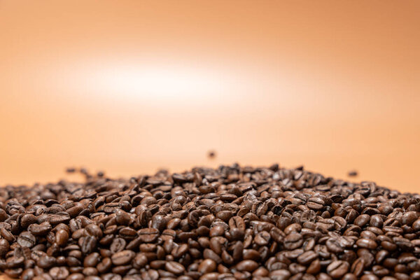 A pile of coffee beans on the table. The beans are brown and on a brown background.