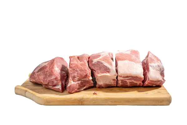 stock image A slab of meat is cut into pieces and laid out on a wooden cutting board. The meat is raw and uncooked, and it is a variety of different cuts. Concept of preparation for cooking Pork meat isolated on white background.