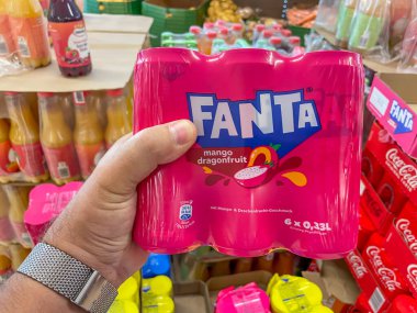 Almanya 23 Ağustos 2024. Adamın biri dükkanda bir kutu Fanta tutuyor. Kutu pembe ve üzerinde bir meyve resmi var. Mağazada Coca-Cola da dahil olmak üzere çeşitli içecekler var..