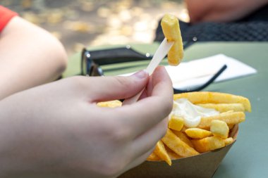 Bir insan çatalla patates kızartması yiyor. Patates kızartması bir kağıt kasenin içinde ve elinde çatal tutuyor.