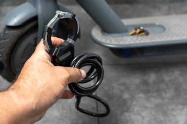 Bir adam elinde elektrikli scooter için kilit tutuyor. Kilit mobiletin arka planına karşıdır..