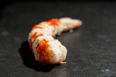 Surimi in the form of shrimps on a black surface. Shrimp come in white and red colors. clipart