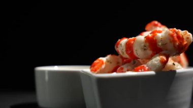 Kırmızı soslu beyaz bir kase ve Surimi 'nin siyah arka planda döndüğü beyaz bir kase. Siyah arka planda kaseler.