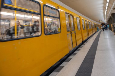 Almanya 15 Eylül 2024. Sarı bir metro treni istasyona yaklaşıyor. Tren insanlarla dolu, bazıları ayakta, bazıları oturuyor. Sahne, Berlin 'e seyahat etmeye hazırlanan insanlarla dolu..