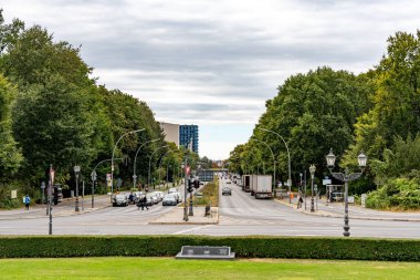 Almanya 15 Eylül 2024. Arabalar ve yürüyen insanlarla dolu kalabalık bir cadde. Sokak ağaçlarla dolu ve arka planda bir park var.