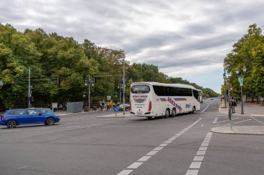 Almanya 15 Eylül 2024. Beyaz bir turist otobüsü caddede ilerliyor. Gökyüzü bulutlu ve cadde ağaçlarla kaplı..
