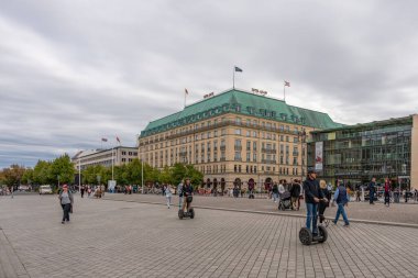 Almanya 15 Eylül 2024. İnsanlar otelin önündeki meydanda yürür ve bisiklete biner. Berlin turizmi. Segways 'e de biniyorlar. İnsanlar kendi işlerine giderken sahne canlı ve gürültülü..