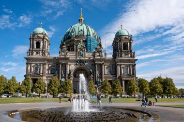 Almanya 15 Eylül 2024. Önünde fıskiye olan büyük bir Berlin Katedrali. Çeşme havaya su püskürtür. Çeşmenin ve binanın etrafında dolaşan bir sürü insan var. Sahne canlı ve gürültülü.