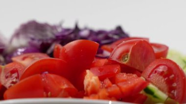 İçinde domates, kırmızı biber ve lahananın da bulunduğu renkli sebze çeşitleriyle dolu beyaz bir tabak. Tabak masanın üzerine yerleştirildi. Salata beyaz arkaplanda döner.