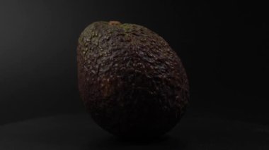 Büyük bir avokado siyah bir yüzeye oturur. Avokado olgunlaştı ve yenmeye hazır. Siyah arka plan avokadonun rengini ortaya çıkarıyor ve öne çıkıyor. Avokado siyah arkaplan üzerinde döner.